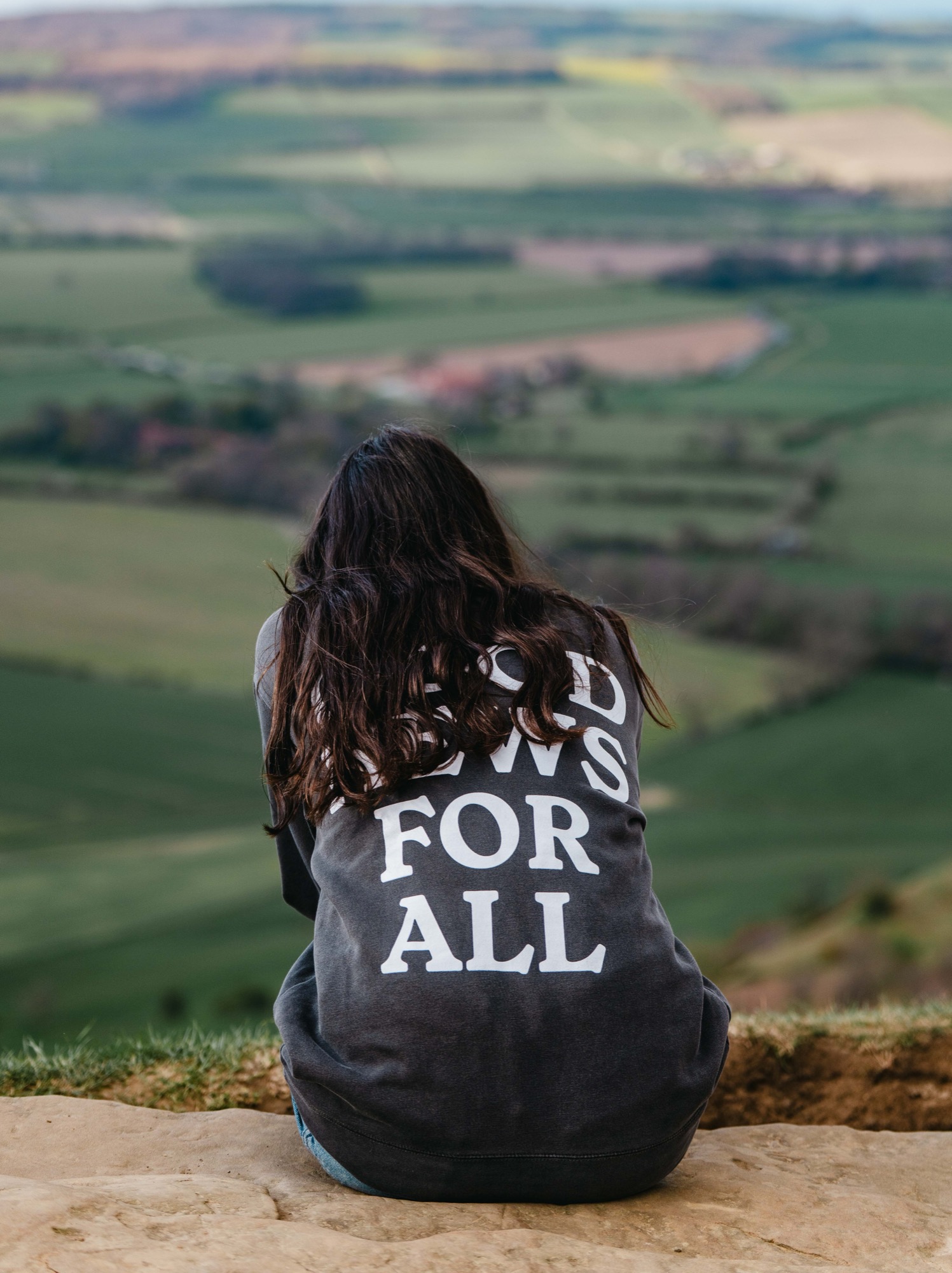 Woman wearing Good News for All shirt overlooking countryside